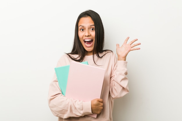 Young hispanic woman holding some notebooks celebrating a victory or success