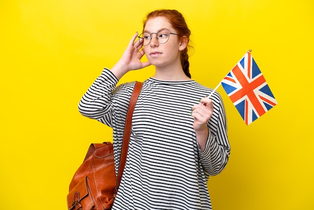 Young hispanic woman holding an United Kingdom flag isolated on yellow background having doubts