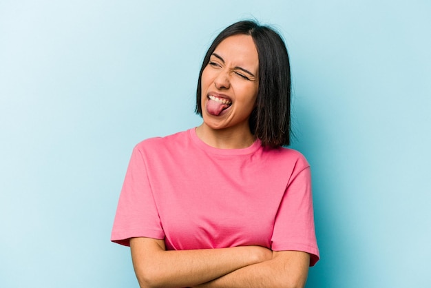 Young hispanic woman isolated on blue background funny and friendly sticking out tongue