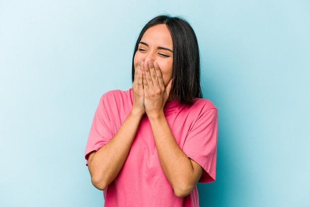 Young hispanic woman isolated on blue background laughing about something covering mouth with hands