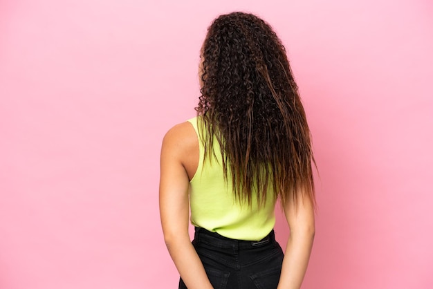 Young hispanic woman isolated on pink background in back position and looking back