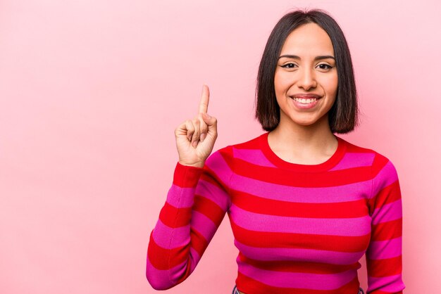 Young hispanic woman isolated on pink background showing number one with finger