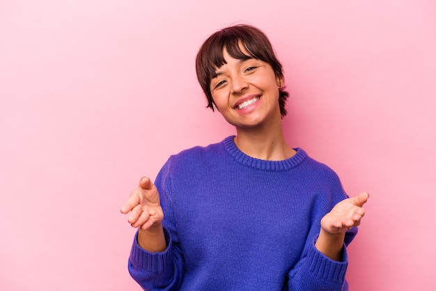 Young hispanic woman isolated on pink background showing a welcome expression