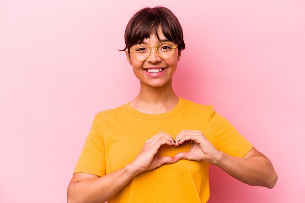 Young hispanic woman isolated on pink background smiling and showing a heart shape with hands