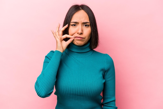 Young hispanic woman isolated on pink background with fingers on lips keeping a secret