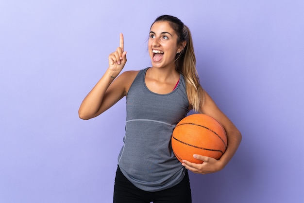 Young hispanic woman over isolated purple wall playing basketball and having an idea