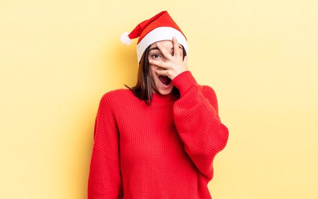 Young hispanic woman looking shocked, scared or terrified, covering face with hand. chistmas and new year concept