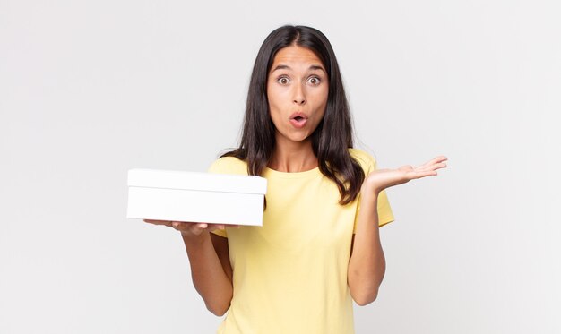 Young hispanic woman looking surprised and shocked, with jaw dropped holding an object