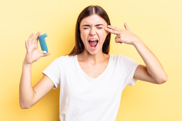 Young hispanic woman looking unhappy and stressed, suicide gesture making gun sign. asthma concept