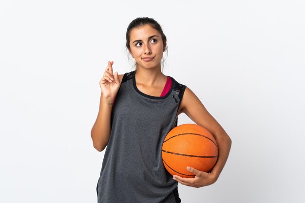 Young hispanic woman playing basketball over isolated white wall with fingers crossing and wishing the best