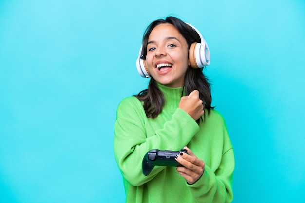 Young hispanic woman playing with a video game controller isolated on blue background celebrating a victory