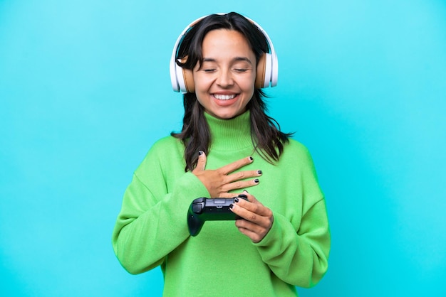 Young hispanic woman playing with a video game controller isolated on blue background smiling a lot