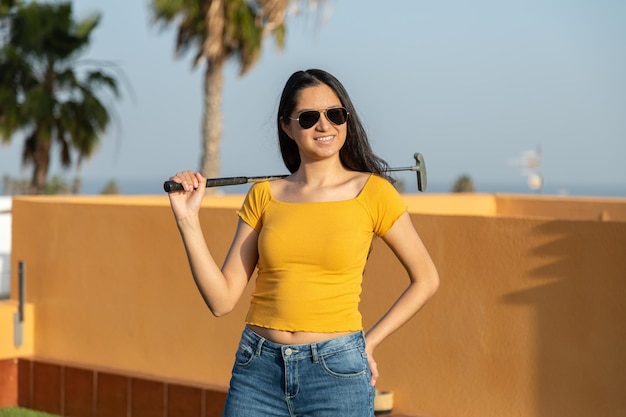 Young Hispanic woman posing with a golf club playing miniature golf