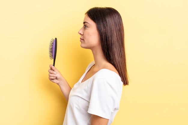 Photo young hispanic woman on profile view thinking, imagining or daydreaming. hair brush concept