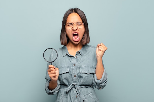 Young hispanic woman shouting aggressively with an angry expression or with fists clenched celebrating success