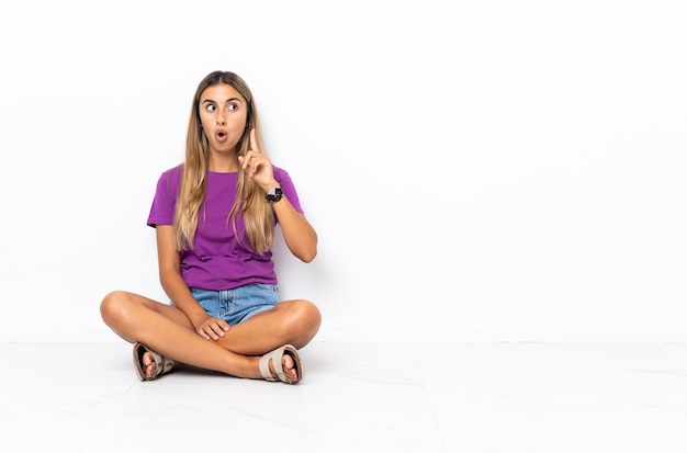 Young hispanic woman sitting on the floor thinking an idea pointing the finger up