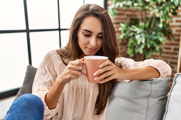 Young hispanic woman smiling confident drinking coffee at home