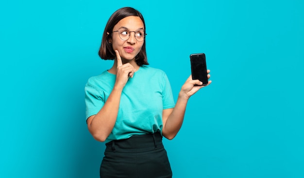 Young hispanic woman smiling happily and daydreaming or doubting, looking to the side