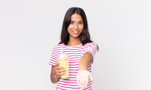 Young hispanic woman smiling happily with friendly and  offering and showing a concept and holding a vanila smoothy milkshake