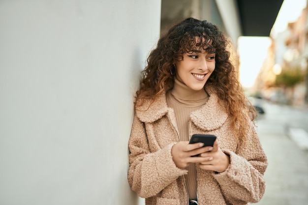 Young hispanic woman smiling happy using smartphone at the city