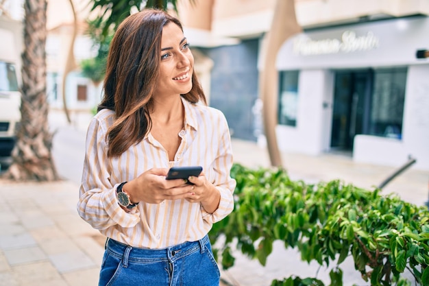 Young hispanic woman smiling happy using smartphone at the city.