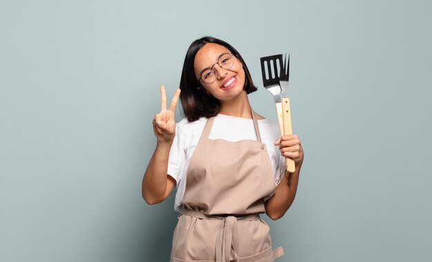 Young hispanic woman smiling and looking happy, carefree and positive, gesturing victory or peace with one hand