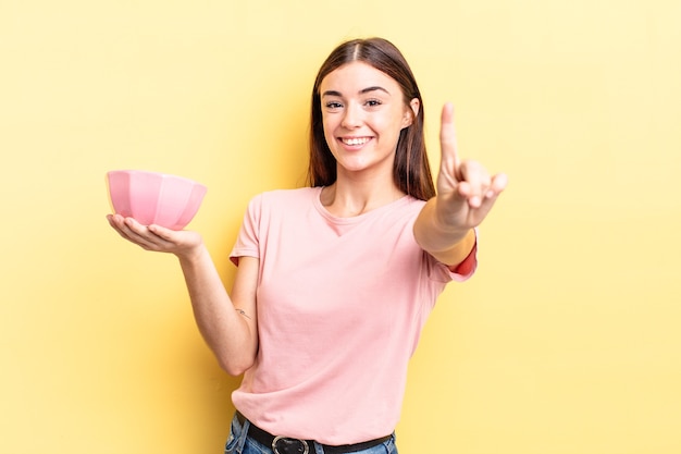 Young hispanic woman smiling proudly and confidently making number one. empty bowl concept