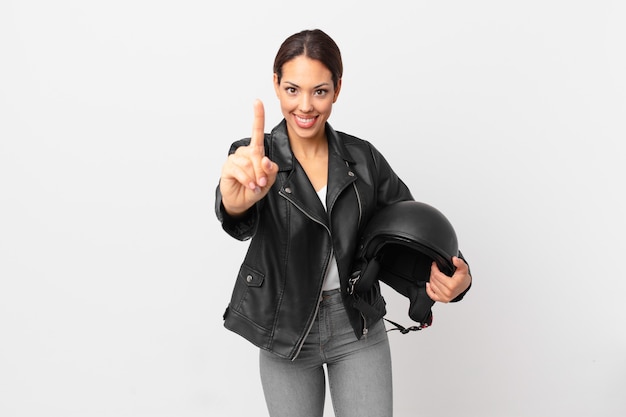 Young hispanic woman smiling proudly and confidently making number one. motorbike rider concept