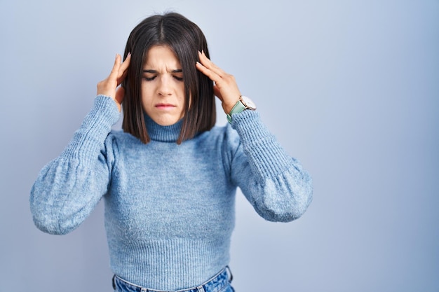 Young hispanic woman standing over blue background with hand on head, headache because stress. suffering migraine.