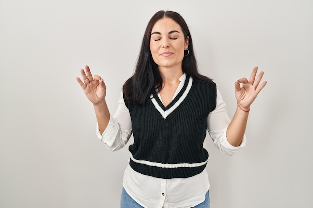 Young hispanic woman standing over isolated background relax and smiling with eyes closed doing meditation gesture with fingers. yoga concept.