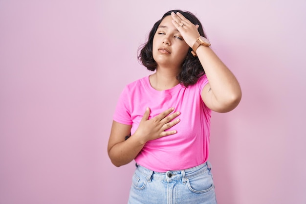 Young hispanic woman standing over pink background touching forehead for illness and fever flu and cold virus sick