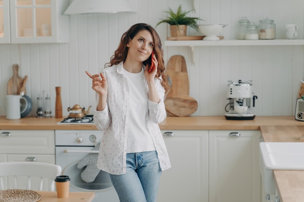 Young hispanic woman talking on phone Relaxed housewife in her stylish kitchen at home