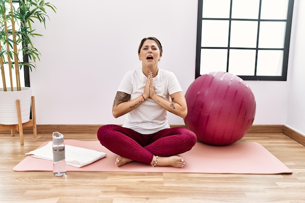 Young hispanic woman training at sport center begging and praying with hands together with hope expression on face very emotional and worried. begging.