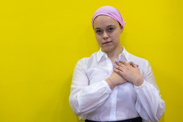 Young hispanic woman wearing breast cancer support pink scarf smiling with hands on chest and grateful gesture on face health concept