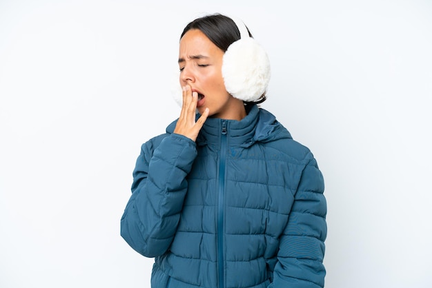 Young hispanic woman wearing a winter earmuffs isolated on white background yawning and covering wide open mouth with hand