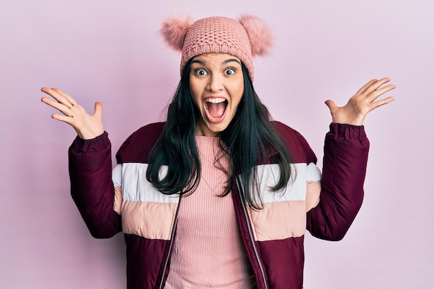 Young hispanic woman wearing wool winter sweater and cap celebrating crazy and amazed for success with arms raised and open eyes screaming excited winner concept