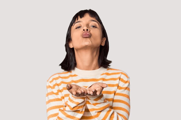 Young Hispanic woman with short black hair in studio folding lips and holding palms to send air kiss