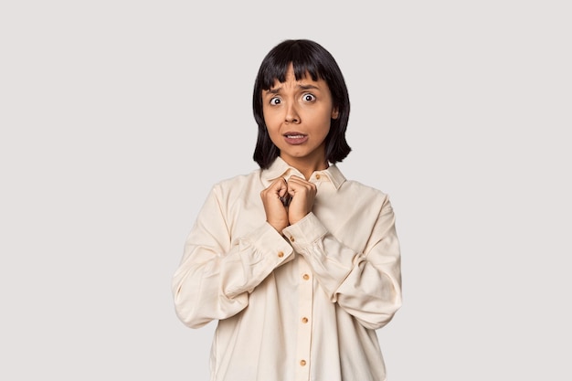 Young Hispanic woman with short black hair in studio scared and afraid