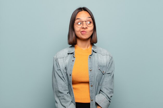 young hispanic woman wondering, thinking happy thoughts and ideas, daydreaming, looking to copy space on side