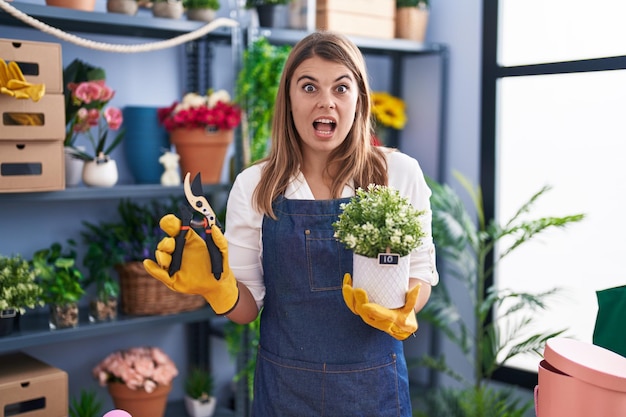 Young hispanic woman working at florist shop afraid and shocked with surprise and amazed expression, fear and excited face.