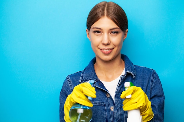 Young housewife wearing yellow rubber gloves holding spray for cleaning home