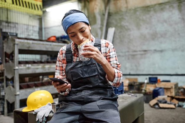 Young hungry hispanic female engineer biting appetizing sandwich