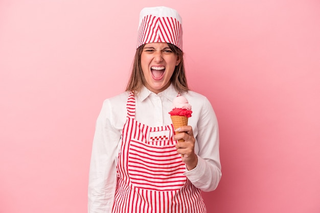 Young ice cream maker woman holding ice cream isolated on pink background screaming very angry and aggressive.