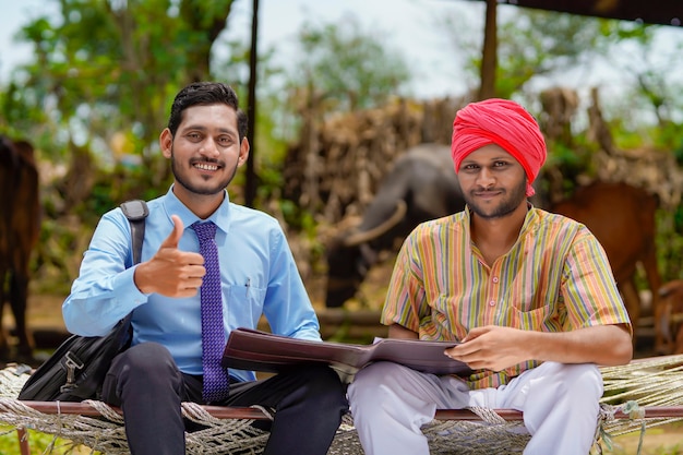 Young india bank officer completing paper work with farmer at his farm.