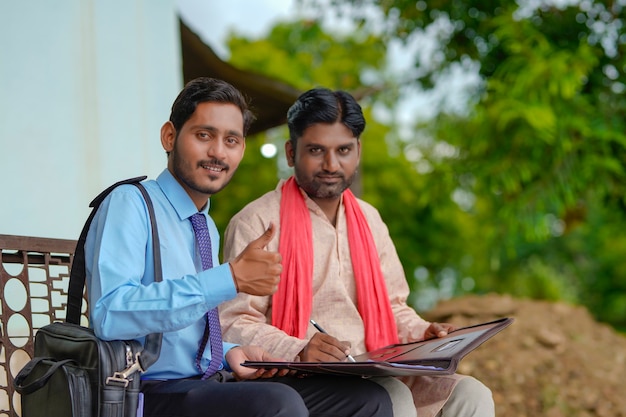 Young india bank officer completing paper work with farmer at his home.