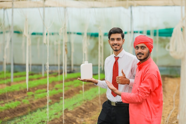 Young indian agronomist and farmer showing bottle at greenhouse