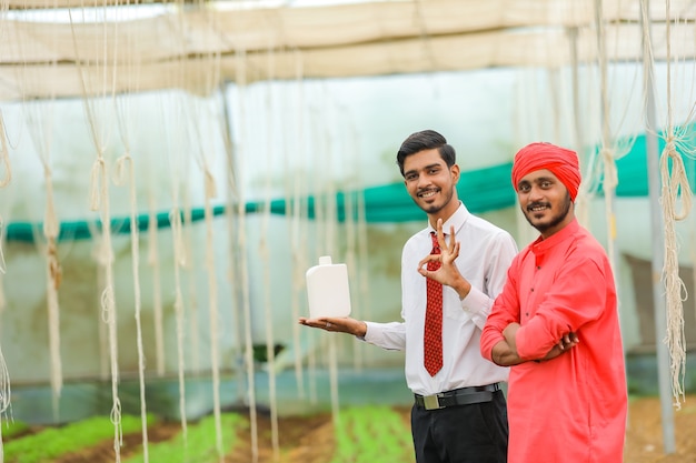 Young indian agronomist and farmer showing bottle at greenhouse