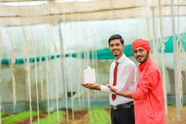 Young indian agronomist and farmer showing bottle at greenhouse