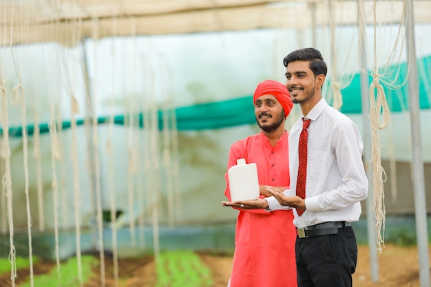 Young indian agronomist and farmer showing bottle at greenhouse