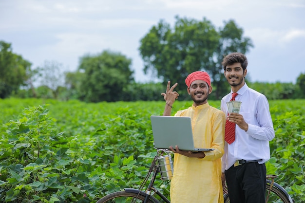 Young indian agronomist showing some information to farmer in laptop at cotton field